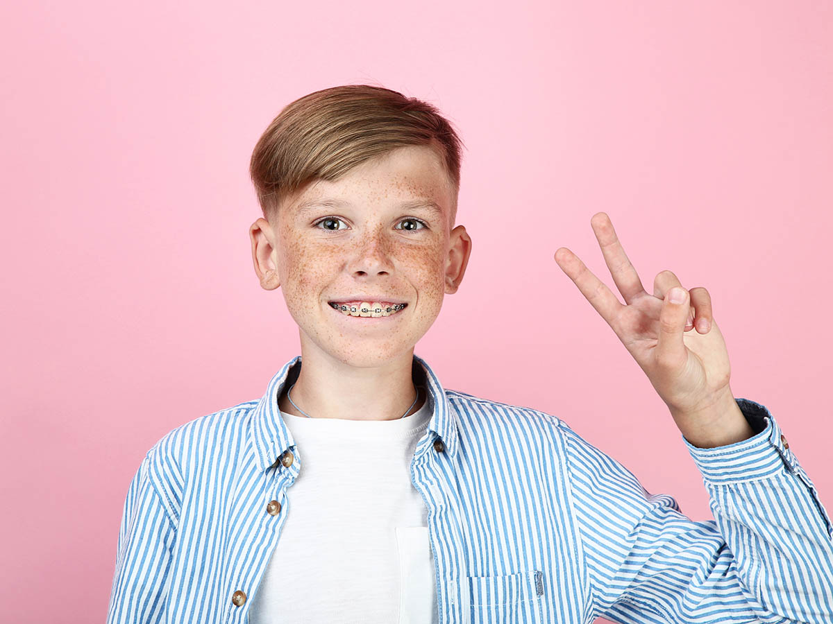 Beautiful young boy with dental braces on pink background